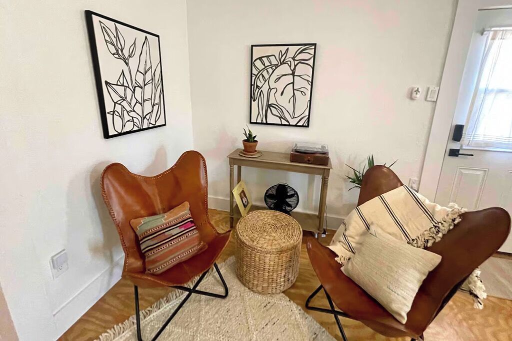 Een woonkamer met twee leren fauteuils, een klein tafeltje met een plant en twee ingelijste kunstwerken aan de muur.
