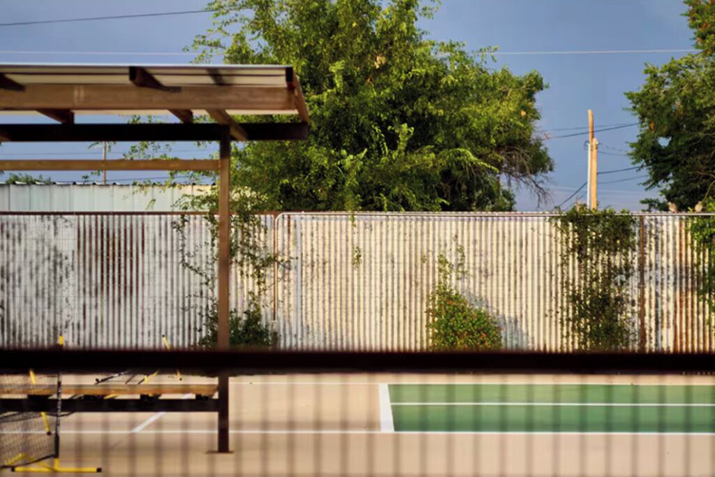 A tennis court with a metal fence and trees in the background.