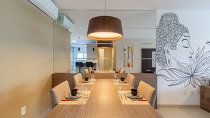 Un espace repas comprenant une longue table en bois, des chaises, une lampe suspendue et une fresque murale.