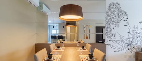 A dining area with a long wooden table, chairs, a hanging lamp, and a wall mural.