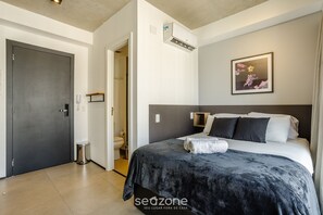Ein modernes Schlafzimmer mit einem großen Bett, einem Nachttisch, einer Wandklimaanlage und einem gerahmten Bild an der Wand.