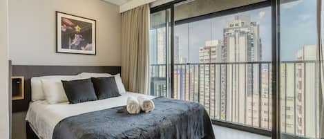 A modern hotel room with a large bed, a city view, and a framed picture on the wall.