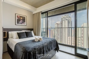 Ein modernes Hotelzimmer mit einem großen Bett, Blick auf die Stadt und einem gerahmten Bild an der Wand.