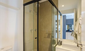 Ein modernes Badezimmer mit einer gläsernen Dusche, einer sichtbaren Toilette und einem Waschbecken mit Handtuchhalter.