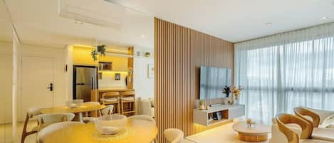 A modern living room with a dining area, a kitchen, and a TV mounted on the wall.