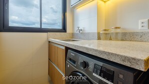 Una cocina moderna con lavadora y secadora integradas, encimera de granito y ventana con vista al cielo.