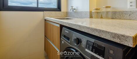 Una cocina moderna con lavadora y secadora integradas, encimera de granito y ventana con vista al cielo.