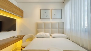 Habitación de hotel moderna con una cama, un escritorio, una silla, un televisor de pantalla plana y dos cuadros en la pared.