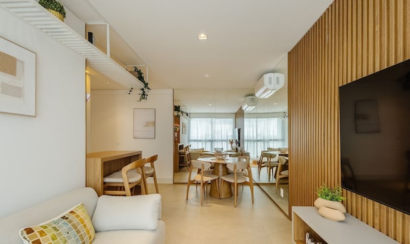 Una sala moderna con un sofá, comedor con sillas y un televisor sobre una pared de madera.