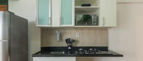 A kitchen with white cabinets, a black countertop, a stainless steel refrigerator, and a microwave.
