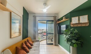 Una sala de estar moderna con un sofá, un ventilador de techo, un ventanal con vista a la ciudad y una pared verde de acento.