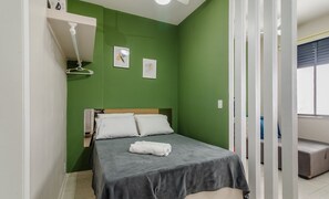 A small, neatly made bed with a grey bedspread and white pillows, a white towel on the bed, and two framed pictures on the green wall. - Studio the City Center 300m Pelourinho Hai0203 (Salvador)