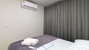 A hotel room with a bed, a grey blanket, a rolled white towel, an air conditioner, and grey curtains. - 2-bedroom Apartment in Asa Norte Nor0101 (Brasília)