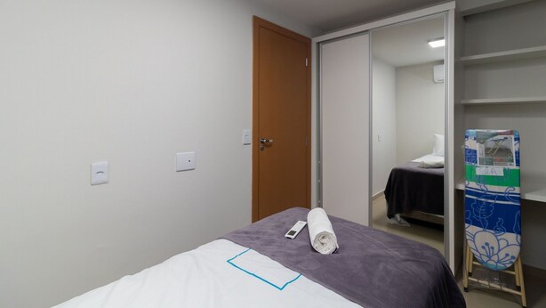 A hotel room with a bed, a wooden door, a mirror, and a shelf with a folded towel and a small item on it. - 2-bedroom Apartment in Asa Norte Nor0101 (Brasília)