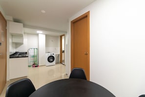 Cocina funcional con estufa, lavaplatos y lavadora. En primer plano, una mesa de comedor con sillas.
