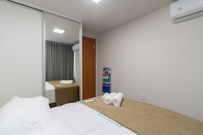 A hotel room with a bed, a small table with towels, a remote control, and an air conditioning unit. - Apart in Asa Norte, 750m From the Mall Nor0201 (Brasília)