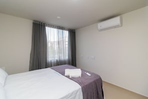 A hotel room with a bed, a window with curtains, an air conditioning unit, and a bedside table with a remote control. - 1BR Apartment, Self-checkin, Asa Norte Nor0202 (Brasília)