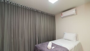 Habitación de hotel con cama, toalla enrollada, control remoto y unidad de aire acondicionado en la pared.