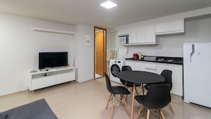 Un espacio habitable compacto con una televisión de pantalla plana, una mesa de comedor con cuatro sillas, lavadora, microondas y refrigerador.