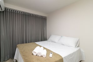Hotellihuone, jossa on sänky, kaukosäädin ja sängyllä rullalle taitetut pyyhkeet.