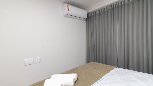 Habitación de hotel con cama, toalla, aire acondicionado y ventana con cortinas.