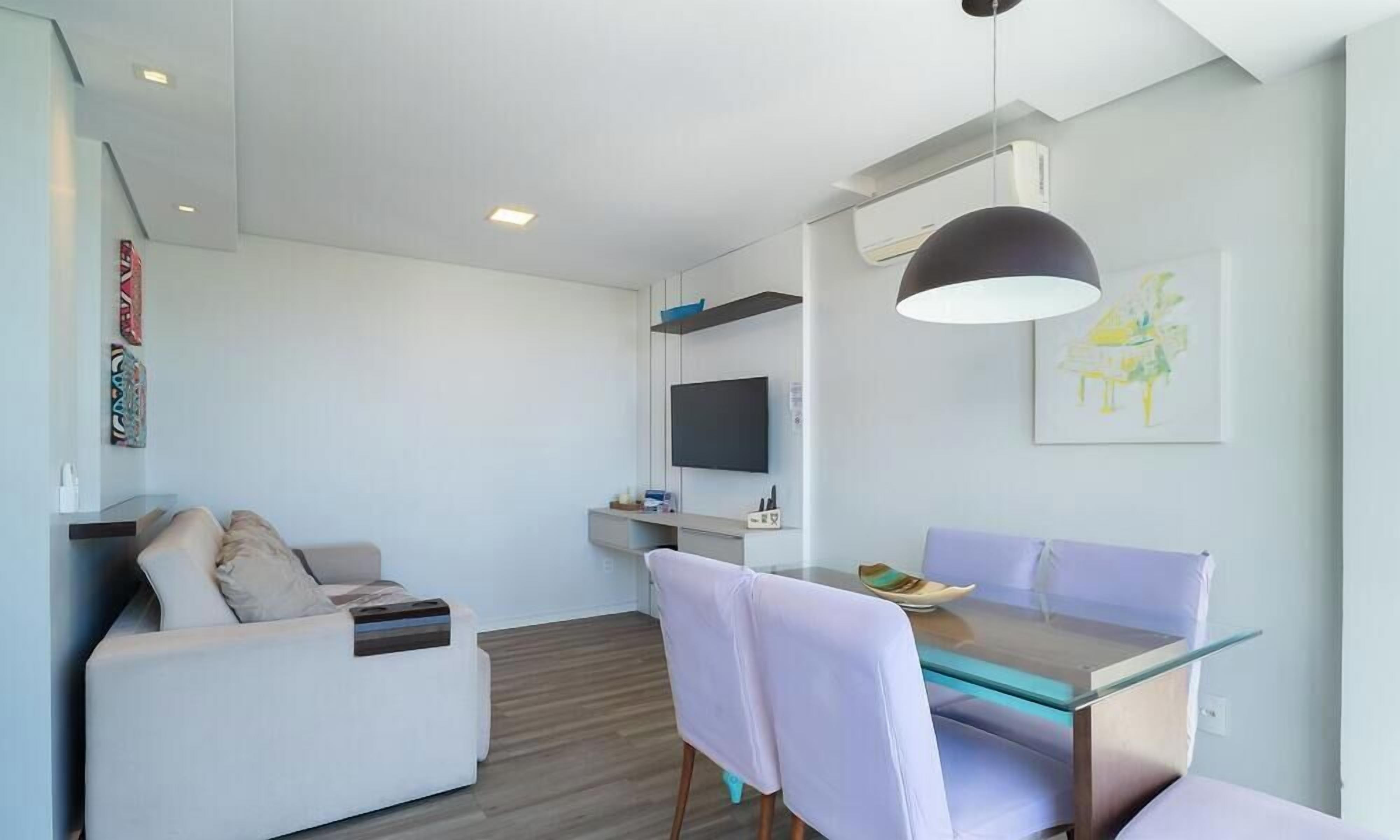 A modern living room with a sofa, a glass dining table, and a TV mounted on the wall.