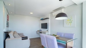 A modern living room with a sofa, a glass dining table, and a TV mounted on the wall. - Practical apt 550m fr Canasvieiras Beach Rtba1361 (Florianópolis)