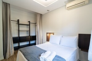 Ein Hotelzimmer mit einem Bett, einem Nachttisch, einer Wandklimaanlage und einer fest installierten Ablagefläche.