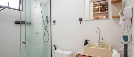 A modern bathroom with a glass shower enclosure, a sink with a mirror above, and a hairdryer mounted on the wall.