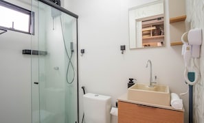 Uma casa de banho moderna com cabine de duche em vidro, lavatório com espelho em cima e secador de cabelo fixado na parede.