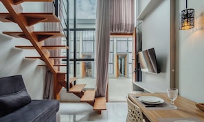 Un interior moderno con una escalera de madera, un sofá, una mesa de comedor con un vaso y un televisor montado en la pared.