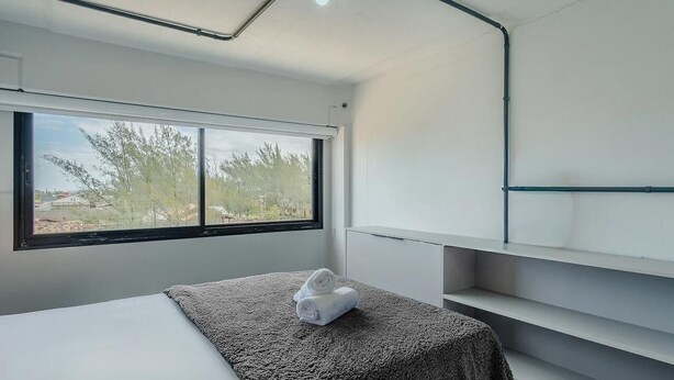 Una camera da letto moderna con una grande finestra, un letto con coperta grigia e un asciugamano bianco sul letto.