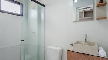 A bathroom with a glass shower enclosure, a white toilet, and a sink with a mirror above it.