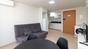 A modern living room with a grey sofa, a dining table, and a kitchen area in the background. - 1BR Apartment, Self-check-in, Asa Norte Nor0203 (Brasília)