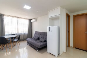 A compact living space with a sofa, a dining table with chairs, a white refrigerator, and a wooden door. - 1BR Apartment, Self-check-in, Asa Norte Nor0203 (Brasília)