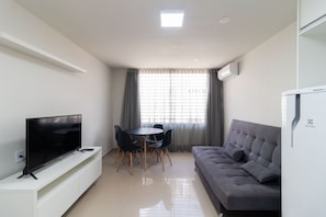 A modern living room with a flat-screen TV, a grey sofa, a dining table with chairs, and a large window with curtains. - 1BR Apartment, Self-check-in, Asa Norte Nor0203 (Brasília)