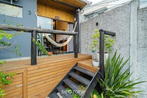 Una terraza de madera con una hamaca, una escalera y una planta en maceta.