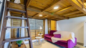 L ’intérieur d’un chalet accueillant, avec un plafond en bois, un canapé violet, une échelle et une petite table sur laquelle est posée une plante.