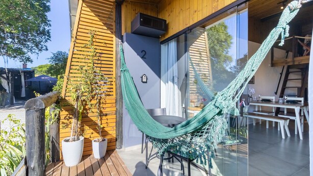 Une terrasse en bois avec un hamac, des plantes en pot et un coin repas comprenant une table et des chaises.