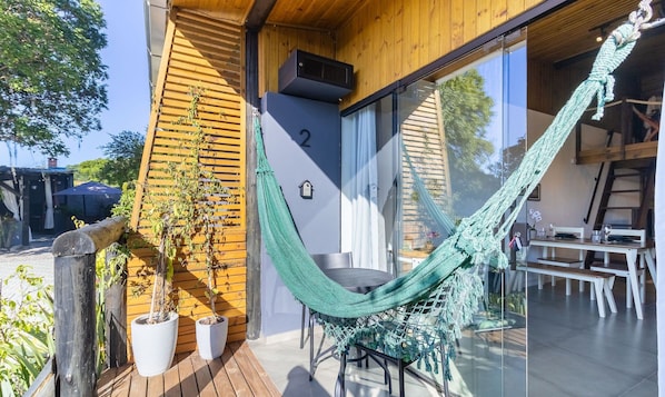 Une terrasse en bois avec un hamac, des plantes en pot et un coin repas comprenant une table et des chaises.