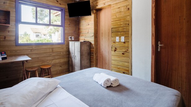 Een kamer met een bed, een bureau, twee krukken, een aan de muur bevestigde televisie en een houten deur.
