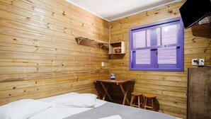Een houten kamer met een bed, een tafeltje, een kruk en een raam met luiken.