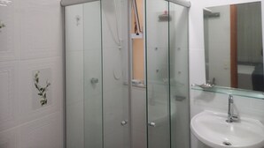 Un bagno con cabina doccia in vetro, un lavandino bianco e uno specchio sopra il lavandino.