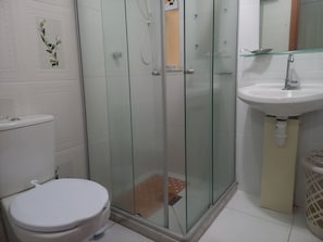 Uma casa de banho com sanita, cabine de duche em vidro e lavatório.