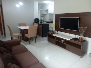 Uma sala de estar com sofá, mesa de jantar e cadeiras, cozinha e televisão sobre um móvel de madeira.