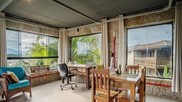 Una habitación con un ventanal grande, un escritorio de madera, una silla de mimbre y un sofá.