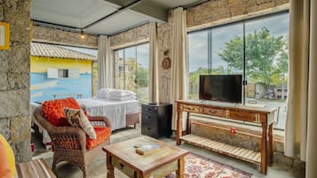 Um quarto aconchegante com uma cama, uma cadeira de vime, uma mesa de madeira e uma televisão.