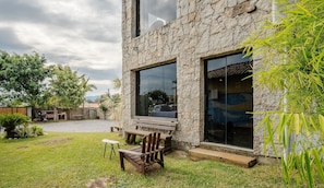 Un edificio de piedra con grandes ventanales, patio cubierto de césped y mesas al aire libre.