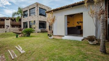 Una casa de dos pisos con fachada de piedra, un balcón y un pequeño jardín con palmeras.