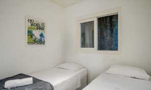 Una habitación con dos camas individuales, un cartel en la pared y una ventana con vistas a un árbol.